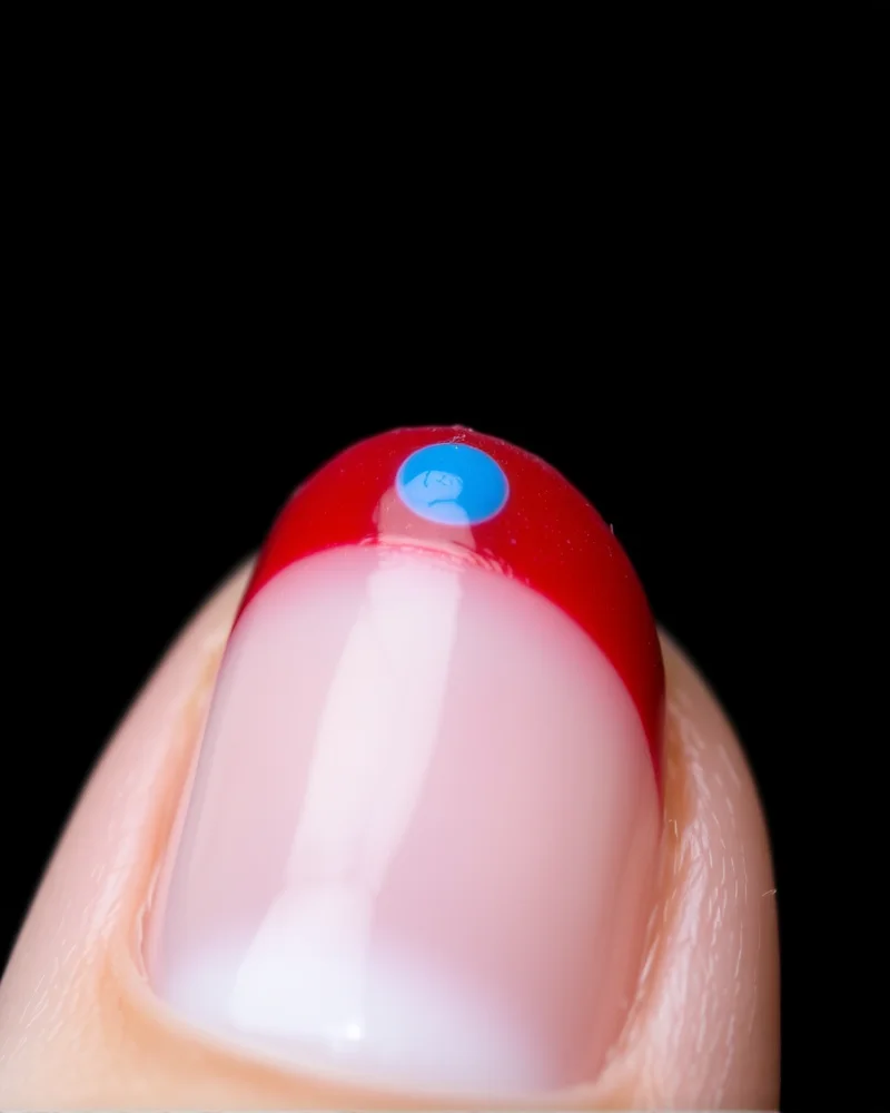 7 Viral 4th of July Nails French Tip Designs You Need to Try 5 Short, rounded nails with a delicate micro-French tip line in red, accompanied by a single blue dot accent.