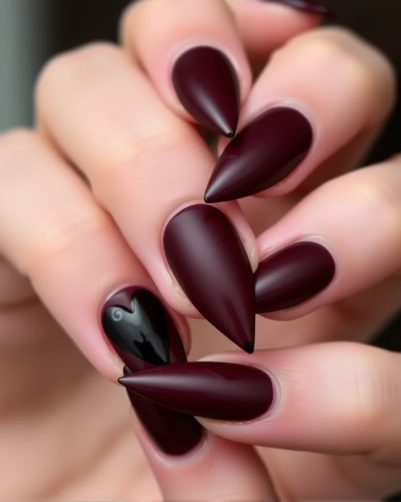 Sharp stiletto nails in matte oxblood with glossy black hearts, showcasing a moody, gothic aesthetic.