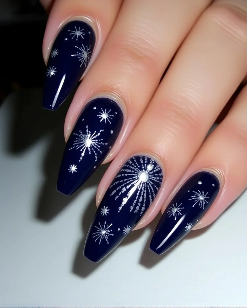 Stiletto-shaped nails painted in deep midnight blue with shimmering silver starburst designs representing fireworks.