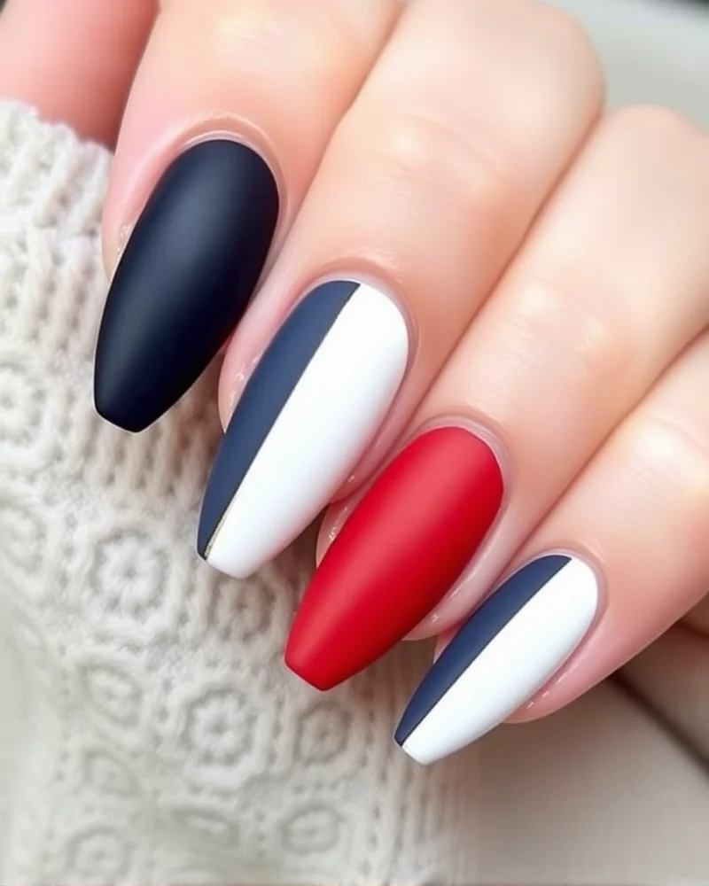 Almond-shaped nails featuring a bold color-blocked pattern of matte red, white, and navy blue with delicate gold foil dividers.